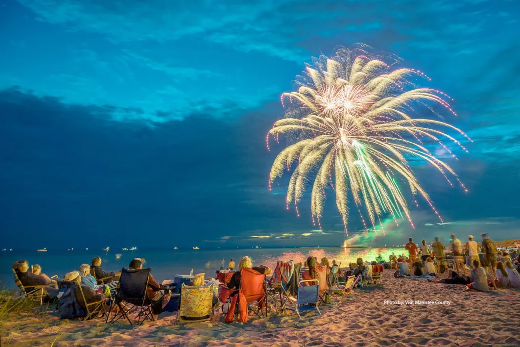 crowd sitting on a beach looking at firework 