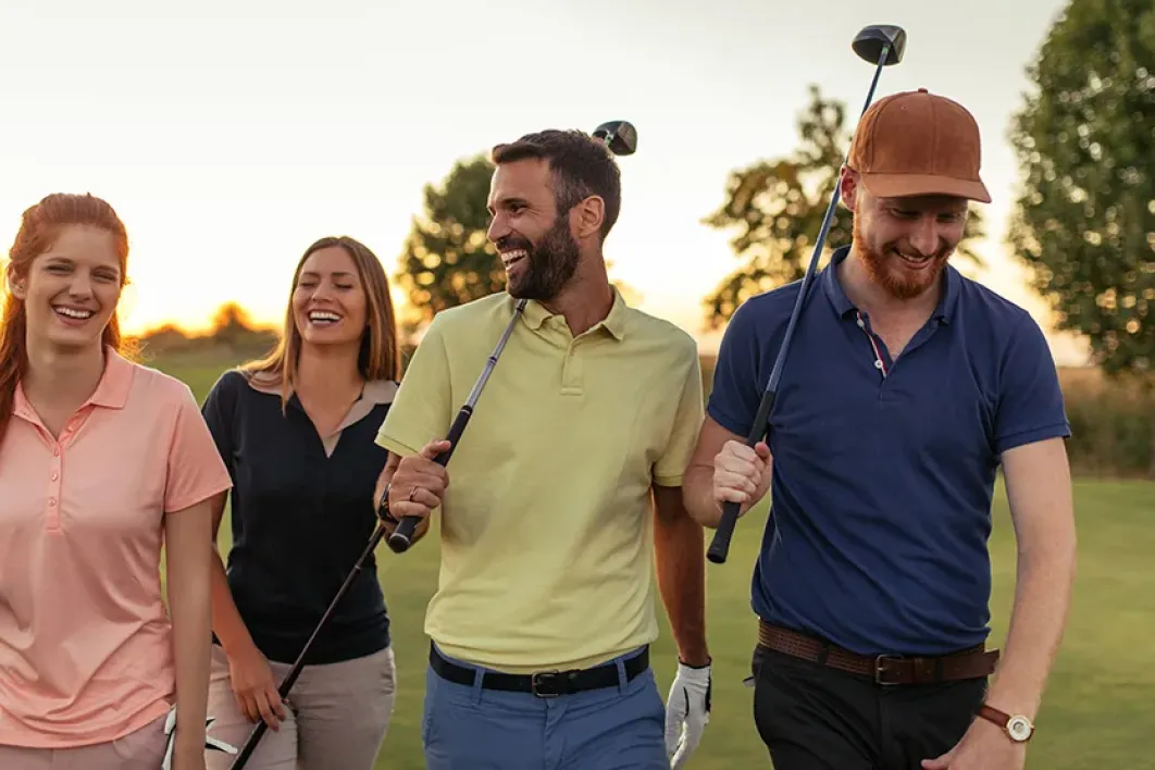 A group of men and women walking and laughing on a golf course 