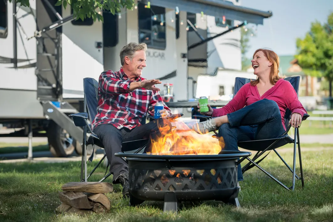 Man and Women in camping chairs in front of a fire pit at Little River RV Park 